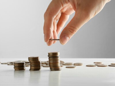 Closeup of a person’s hand stacking coins on a table.
